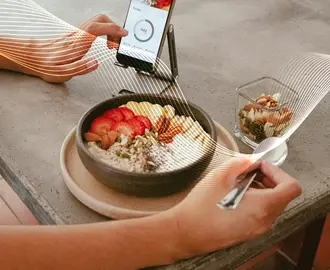 A person eats a healthy breakfast while looking at a phone app