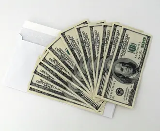 10 one hundred dollar bills fanned out on top of a white envelope