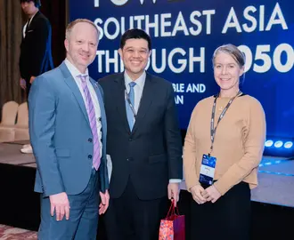 Three people smile and pose for a picture in front of a stage
