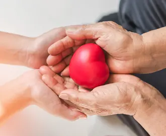 Two pairs of hands holding a red heart