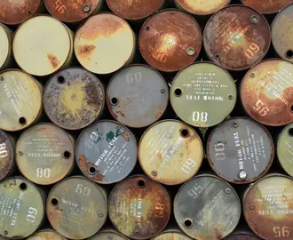 Pile of old, rusty oil barrels stacked outdoors with visible labels and numbers.