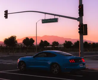 Blue sports car at a road intersection during sunset with a mountainous backdrop.