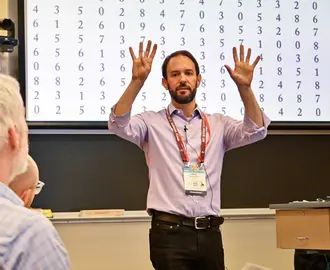 A man gestures while standing in front of a classroom