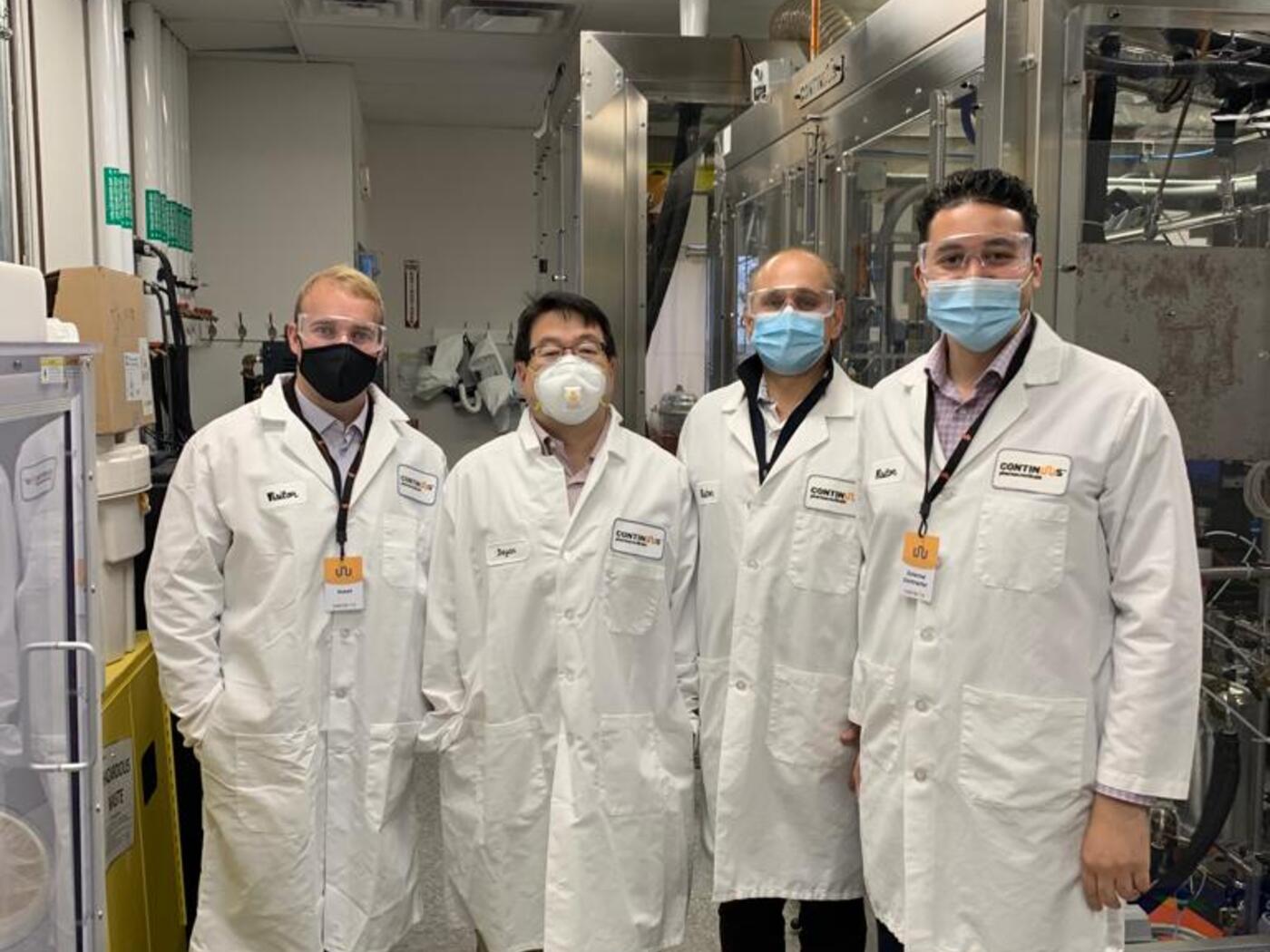 Three H-Lab students and Bayan Takizawa posing in lab coats at Continuus Pharmaceuticals