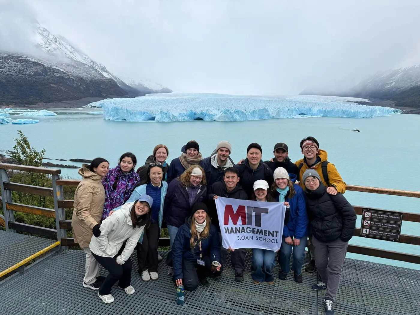 Study tour attendees pose in a group photo in front of a glacier holding an MIT sign
