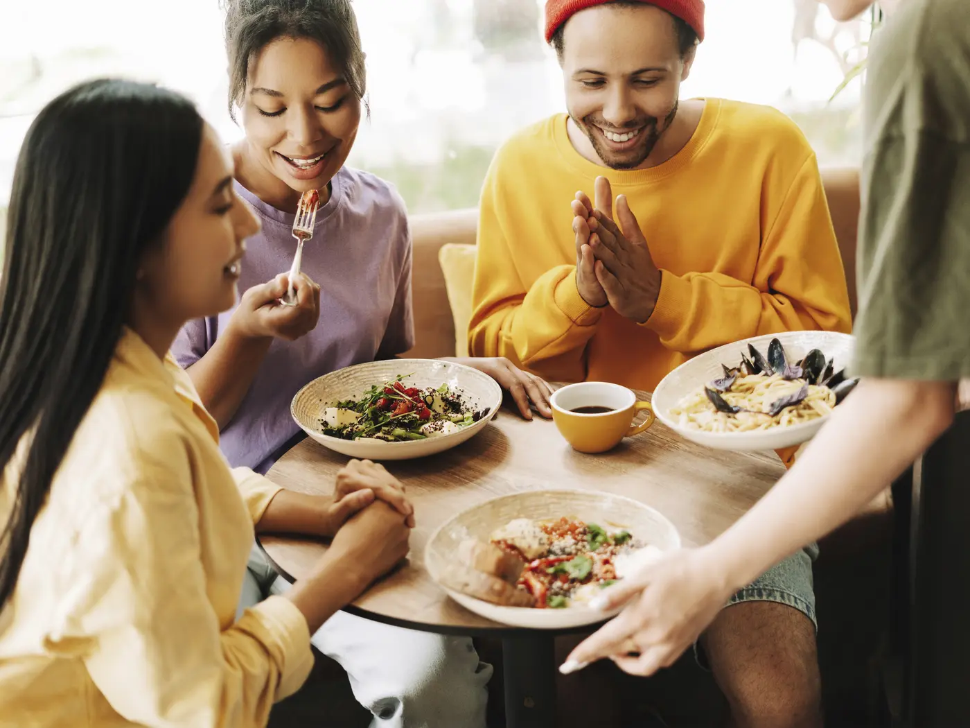Waitress bringing food to a group of three friends in a restaurant.