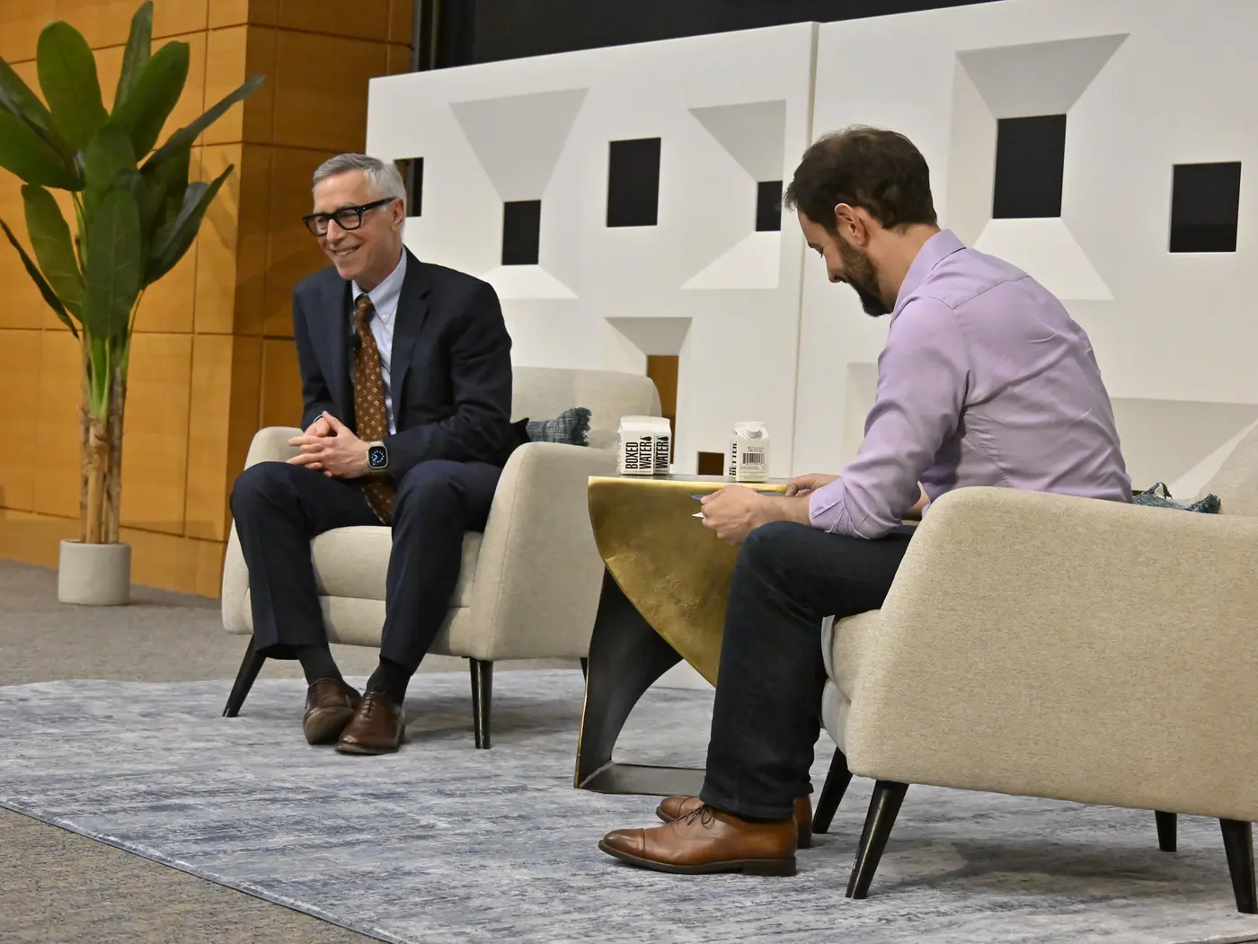 Two men laugh during a fireside chat.