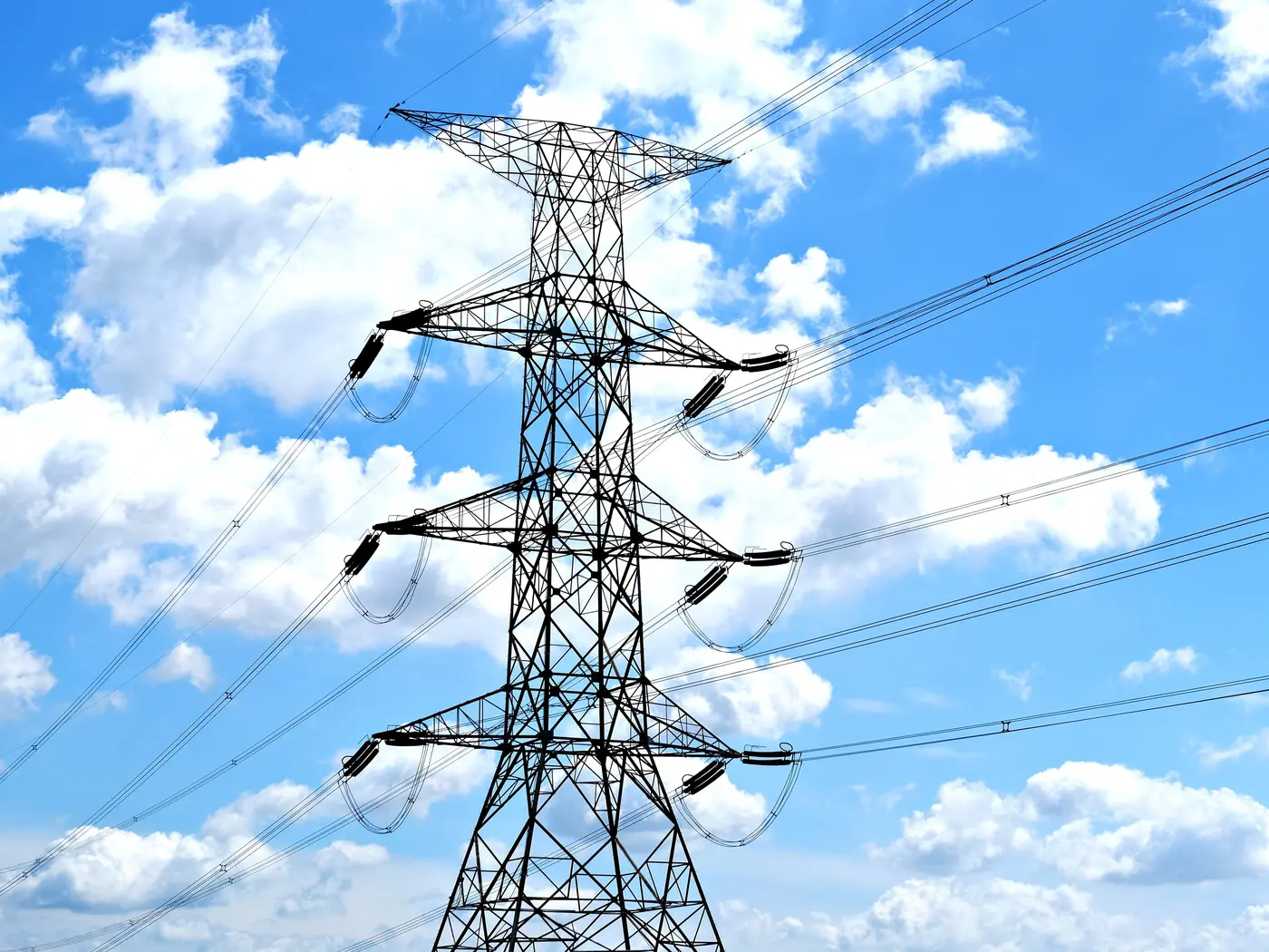 Electricity pylon with high voltage lines set against a vibrant blue sky with clouds.