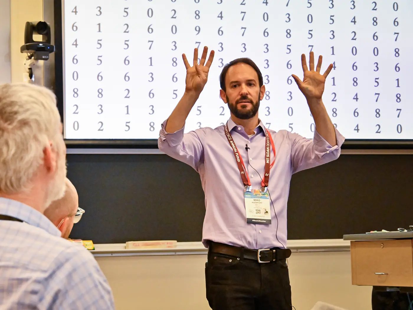 A man gestures while standing in front of a classroom