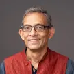 Photo of a person with short gray hair and glasses wearing a gray shirt and dark orange vest