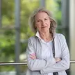 Picture of a person with long grey hair wearing a white shirt and a light grey jacket