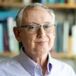 Photo of a person with short grey hair wearing glasses and a blue shirt