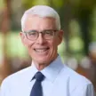 Man with white hair wearing blue shirt, blue tie, blue glasses