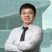photo of a man weating a gray shirt, dark tie and wire-rimmed glasses against a blurred building background
