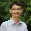 photo of a man wearing a blue striped shirt and black-rimmed glasses against a blurred background of trees
