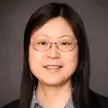 Woman with dark hair and glasses wearing wire-rimmed glasses, a dark jacket, and a blue checked shirt