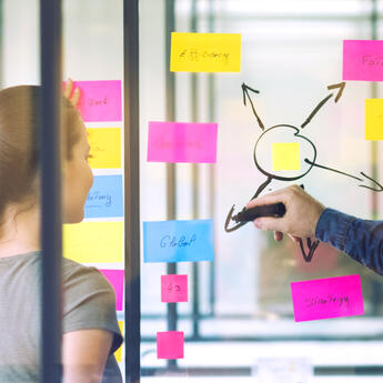 A person draws on a glass board with various sticky notes