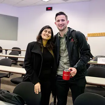 Two students standing in a classroom smile for a photo.