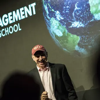 Professor Rigobon speaks to an audience in front of a screen with the MIT Sloan logo
