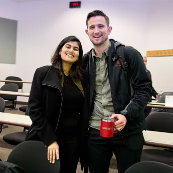 Two students standing in a classroom smile for a photo.