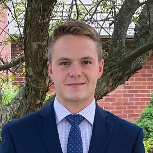 Portrait of Tom Kyle in front of a tree, wearing a suit and tie.