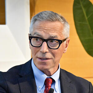 A man in glasses and wearing a suit speaks in an auditorium