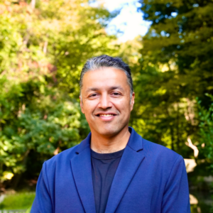 Man in blue suit smiling while posing for photo outside