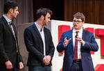 three men in suits stand on a stage
