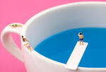 miniature diver perched on a coffee cup with blue water