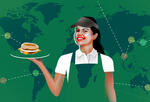 Barista in green apron holding breakfast sandwich in front of supply chain map