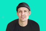 Mikkel Christopher smiles at the camera with a mint green background