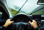 view from the driver's seat of two hands on a steering wheel and a rainy mountain road