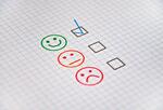 Happy, neutral, and sad faces on a piece of paper with checkboxes next to each, representing product rankings and consumer feedback.