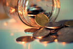 A photograph of a glass jar on a table with coins falling out