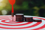 A dart arrow hitting the center of a dart board with coin stacks