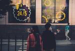 Image of two people with masks standing outside a business with a sign that says "open 24/7"