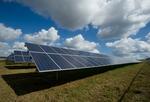 Solar panels in a field under a blue sky with clouds.