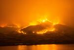 Image of a wildfire coursing across mountain tops at night, by a body of water.