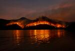 wildfires burning behind a body of water at night